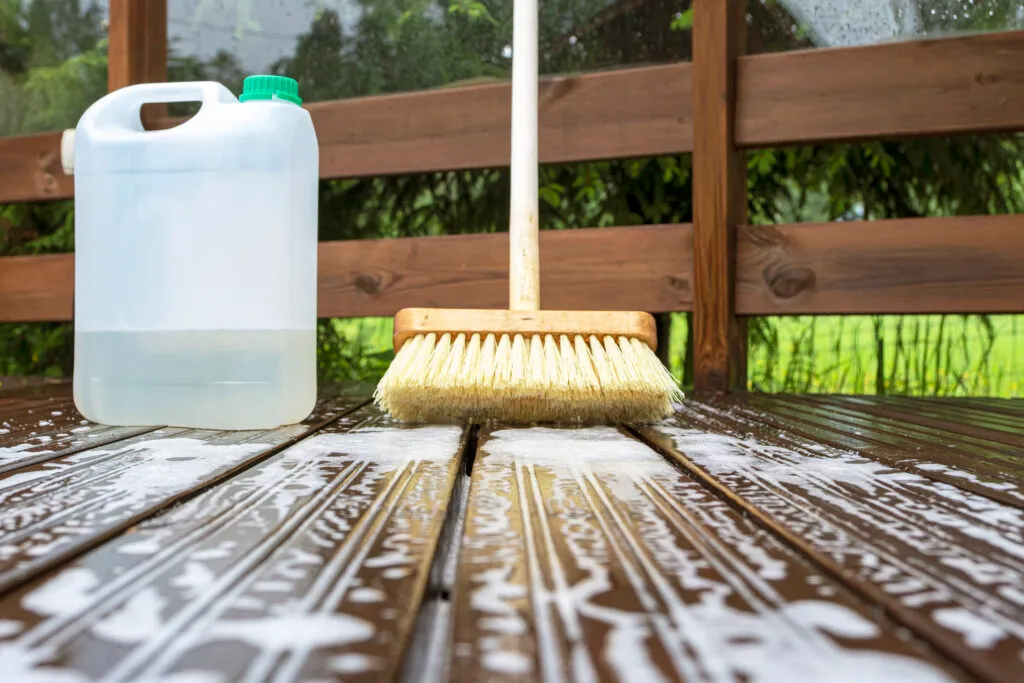 Brush, plastic canister with mortar and soapy water on wooden terrace boards.