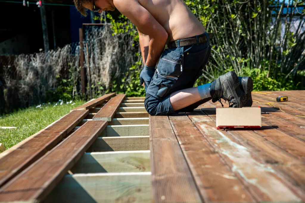 Deck construction builder hand with electric screwdriver installing impregnated wooden boards 2
