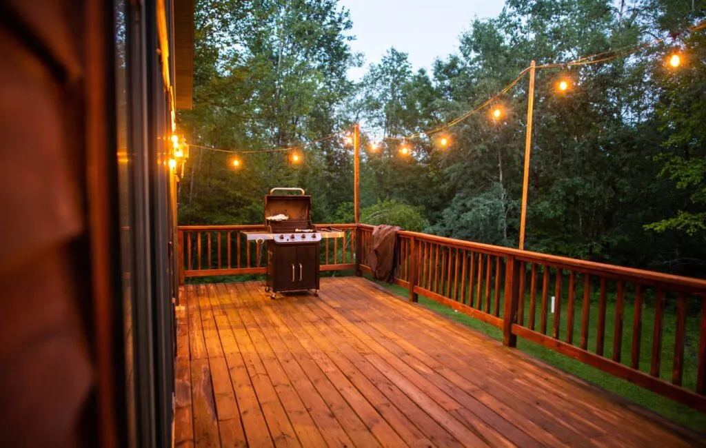 A wooden porch with string lights and grill